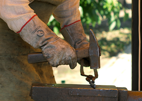 Person wearing thick gloves forging a knife