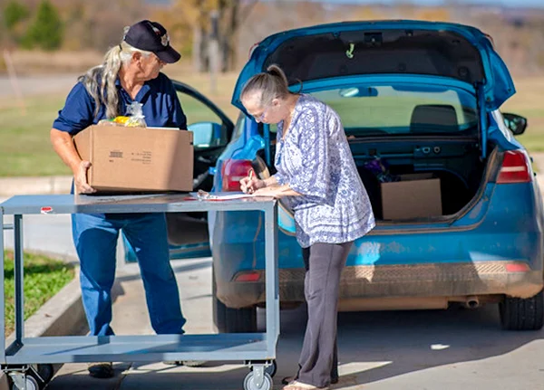 Man helps woman load a box into the trunk of car