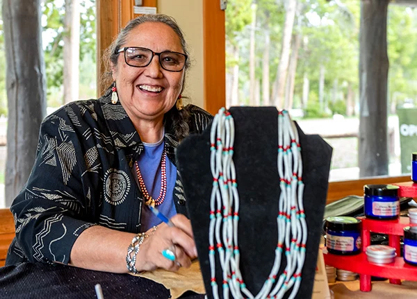 Woman sitting at a table displaying a necklace and smiling