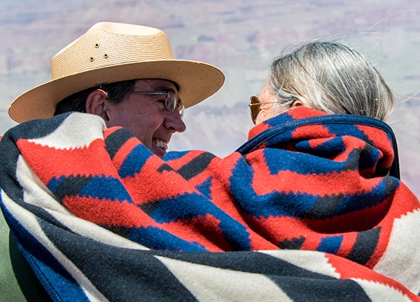 An older couple sitting together looking at each other with a blanket wrapped around them