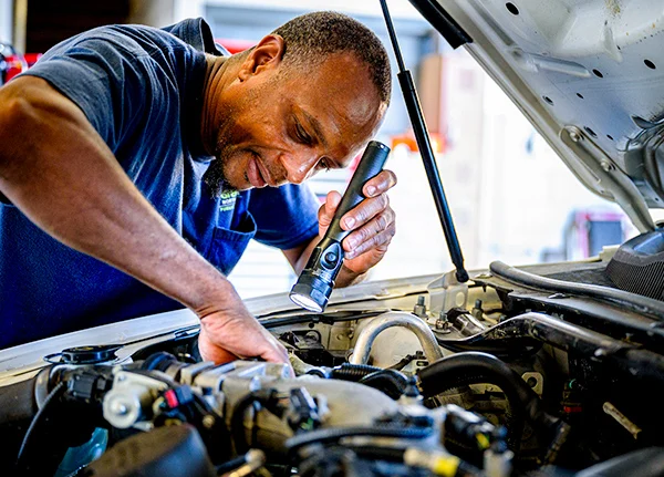 Mechanic holding flashlight and looking under the hood of a car