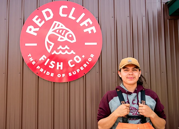 Young person standing in front of a Red Cliff Fish Co sign on a building