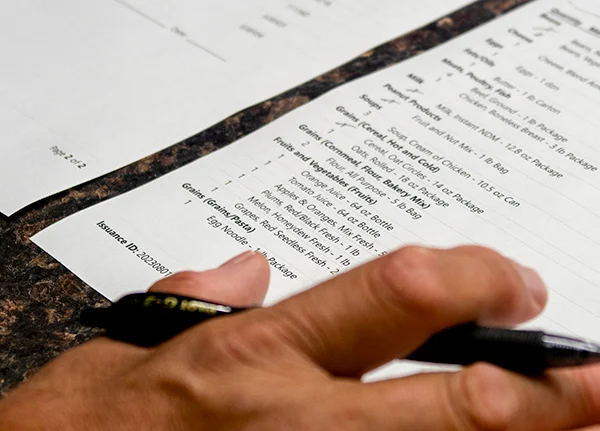 Hand holding a pen next to a paper with a list of inventory