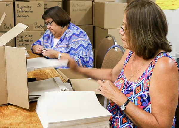 Two women packaging boxes in a supply room