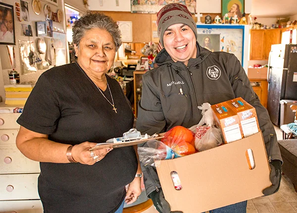 Woman holding a clipboard and man holding a box of food stand next to each other smiling