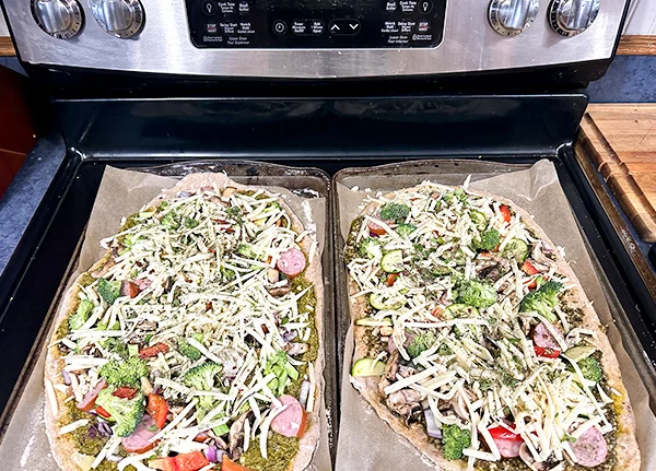 Homemade, uncooked pizzas on pans on top of an oven