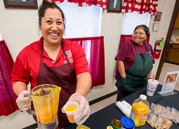 Woman holding a blender and a fruit smoothie and smiling
