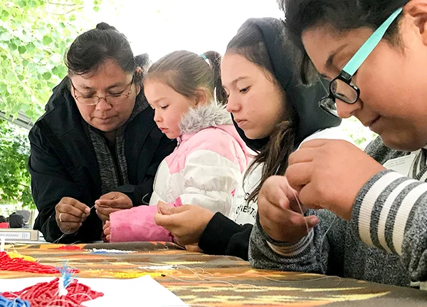 Woman showing three young girls how to bead