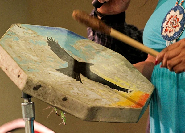 Person drumming on a drum with a painted bird on it