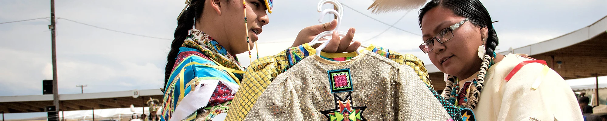 Two people looking at ceremonial clothing on hangers