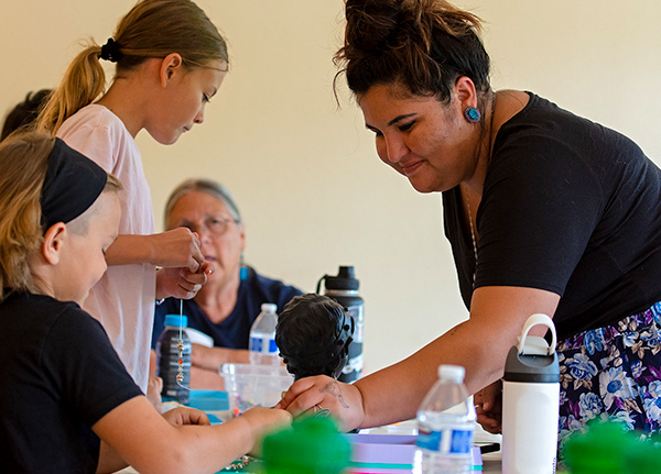 Woman helping young girls make beaded bracelets