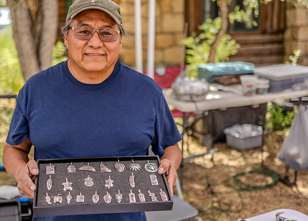 Man holding a display case with silver pendants in it
