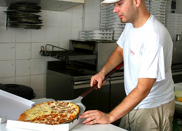 Man slides pizza into a box using a pizza peel