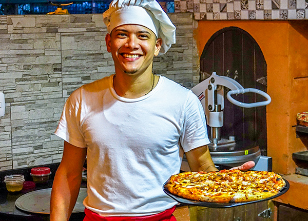Man wearing a chef hat and holding a pizza