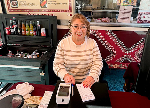 Woman sits at a table in front of a food truck with a point of sales system and an order pad