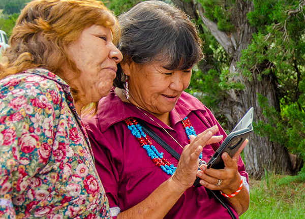 Two older women stand next to each other looking at something on a phone screen