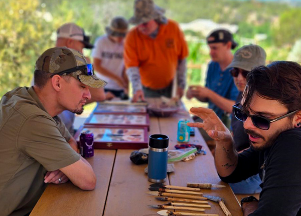 A group of people sit around a table looking at arrowheads and knives