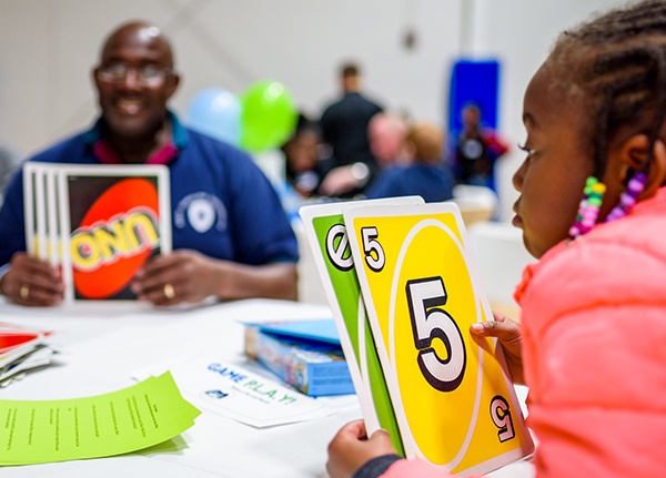 Young girl sitting at a table with a man playing Uno with jumbo cards