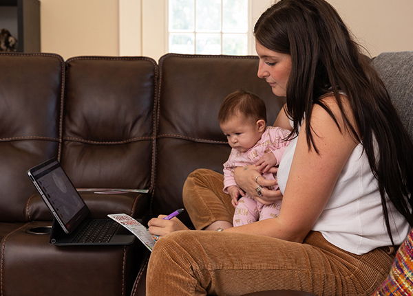 Woman sitting on a couch with a small baby while typing on a laptop