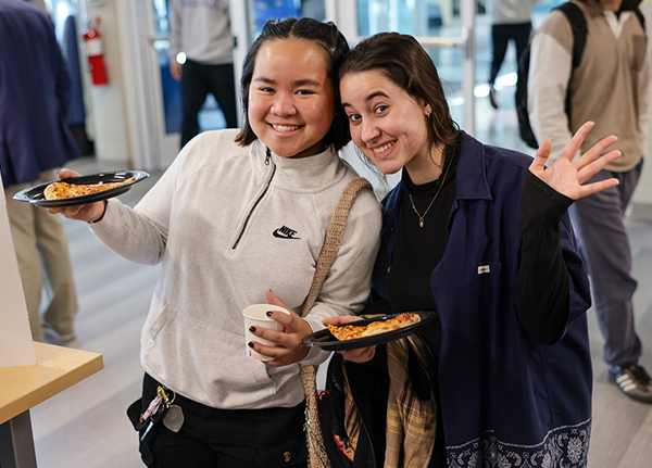Two young women holding pizza and smiling at the camera