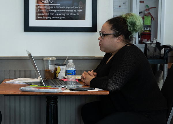 Person sitting at a table with their hands crossed in front of a laptop