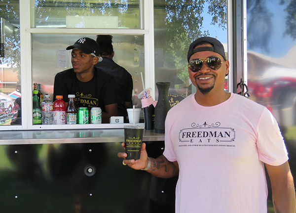 Man standing in front of a food truck holding a cup and wearing a shirt with the same logo