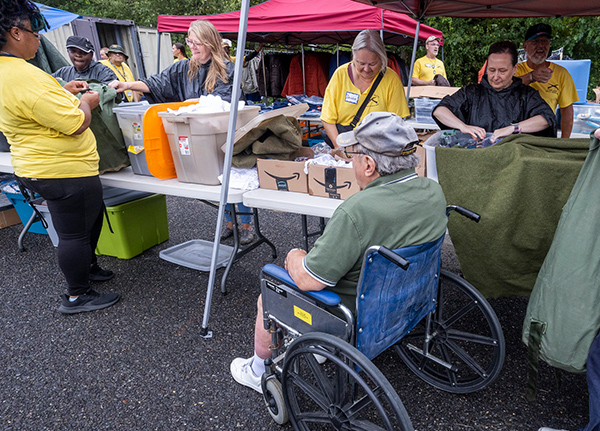 Man who uses a wheelchair at an outdoor event with people setting up in the background