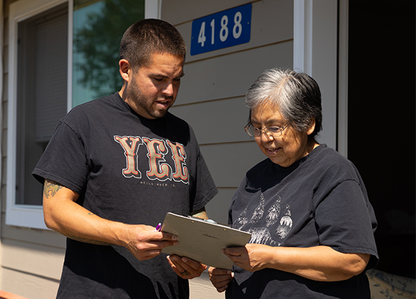 Two people standing on a porch looking at a clipboard