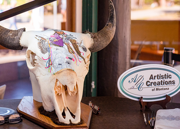 A painted cow skull with a sign that says Artistic Creations of Montana