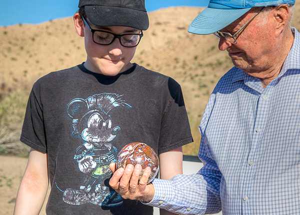 Older man showing a younger boy a rock that he's holding