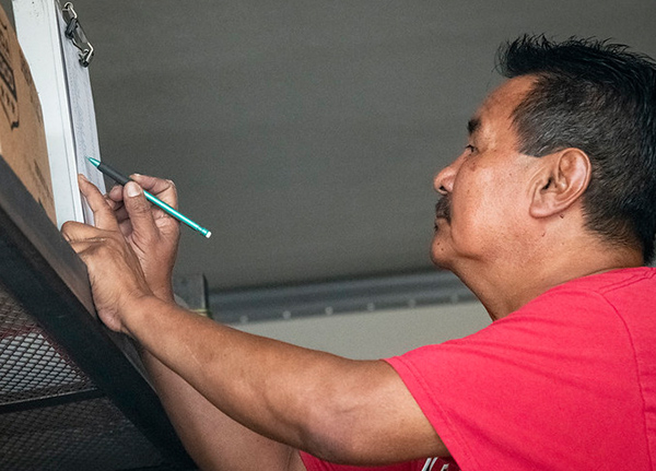 Man writing on a clipboard against a box on a shelf