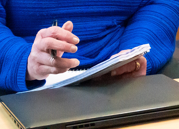 Person writing in a notebook on top of a closed laptop