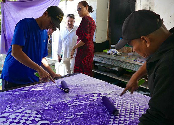 A small group of people rolling ink on a large printing block laid out on a table