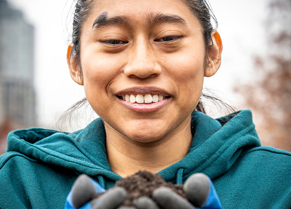Young person wearing work gloves holding a pile of soil