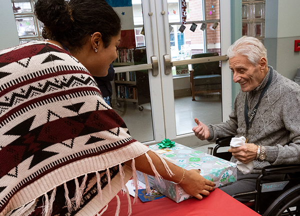 Woman handing wrapped gift to an older man who uses a wheelchair