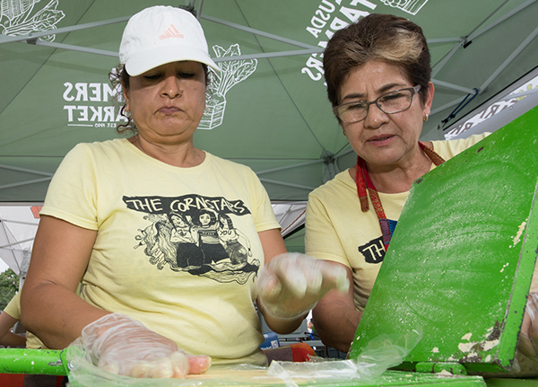 Two women making food at an outdoor market stand