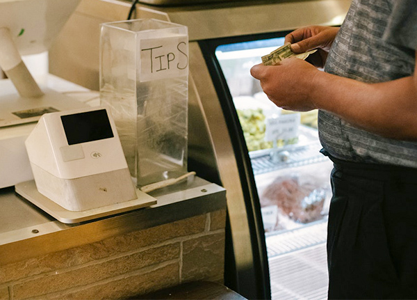 Person standing in front of a counter with a display case and point of sales system in the background