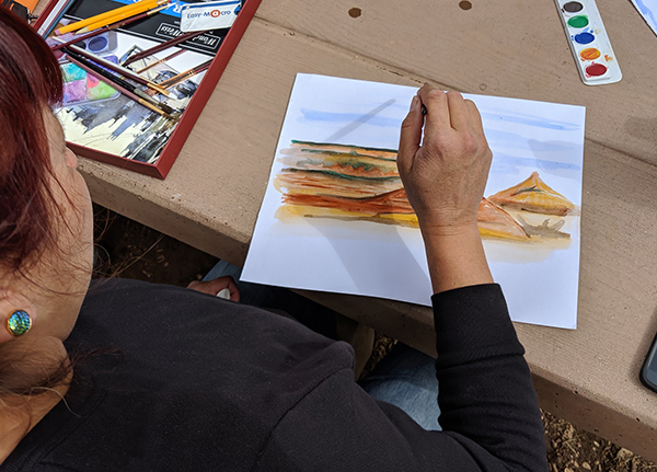 Person painting a scenic landscape with watercolors