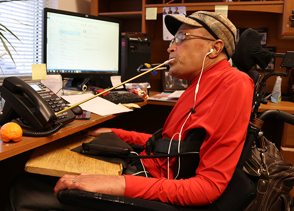 Man at a desk using a mouth stick to dial a phone number