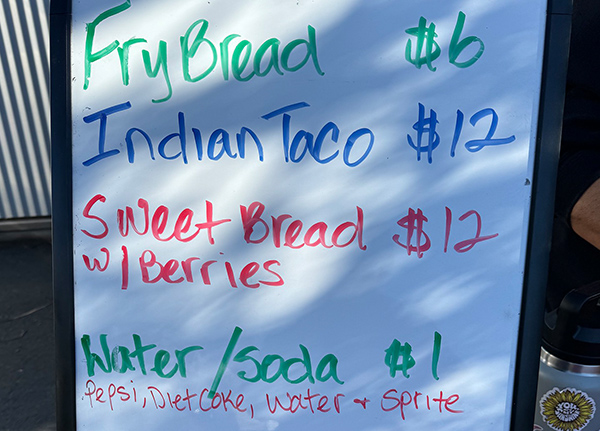 A menu written on a whiteboard with frybread and Indian taco prices