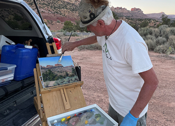 Man painting a landscape out of the back of his vehicle