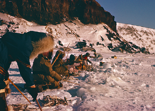 Traditional fishermen with spears kneel in the snow