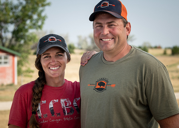 Two people wearing baseball caps and t-shirts standing next to each other smiling for the camera