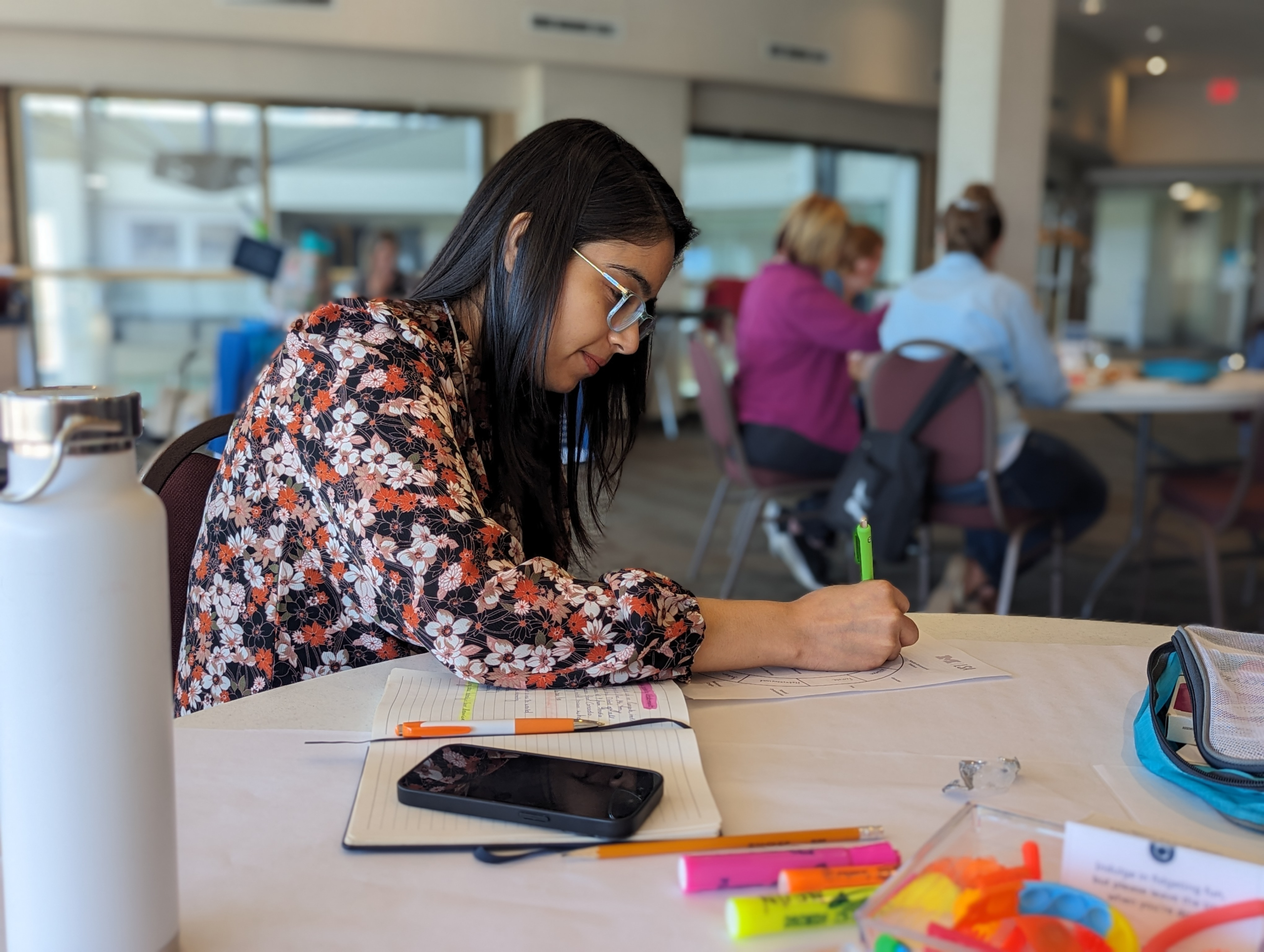 Person writing on a piece of paper with a notebook and phone on the table